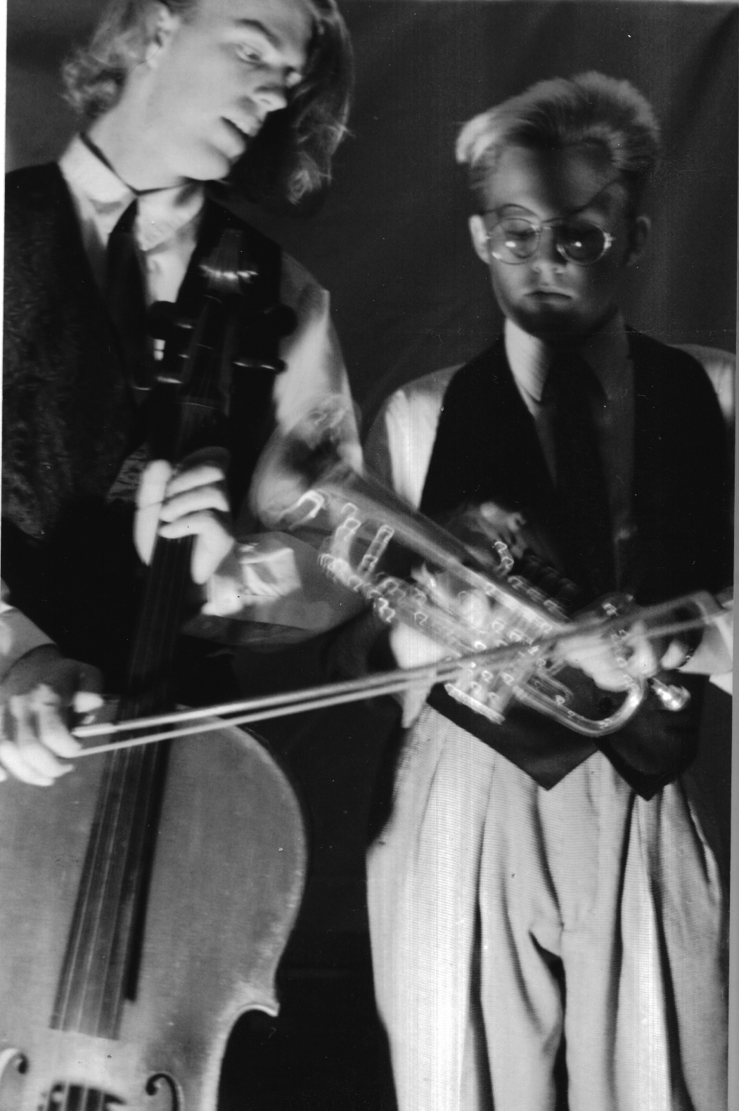 Distressed black-and-white photograph of two young musicians in vests and ties, one with a cello and one with a trumpet, blurred by a double exposure