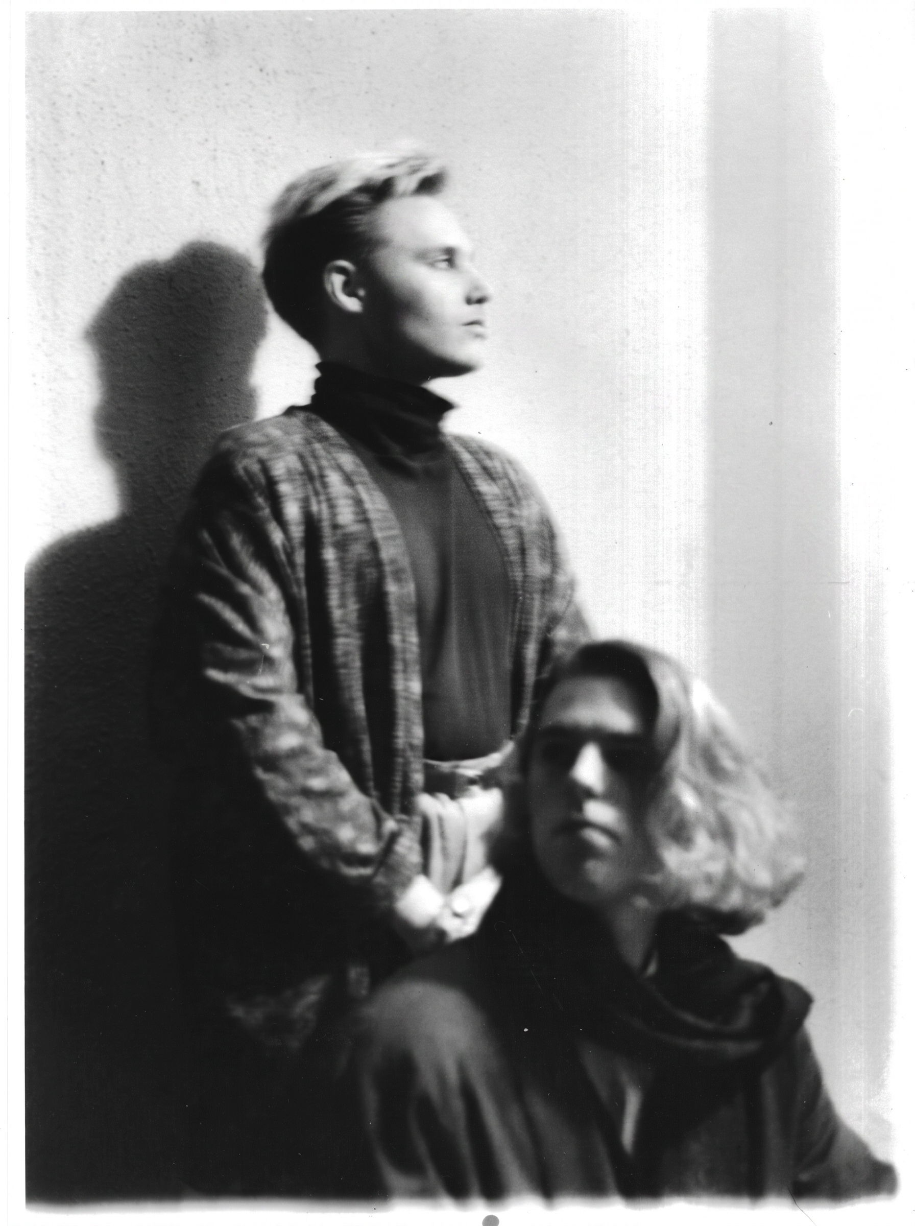 Restored distressed black-and-white photograph of two figures against a pale wall, with the original diagonal pen mark removed