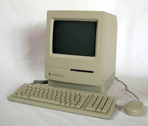 Vintage beige all-in-one desktop computer with small monochrome screen and floppy drive, yellowed with age, photographed against a grey archival background